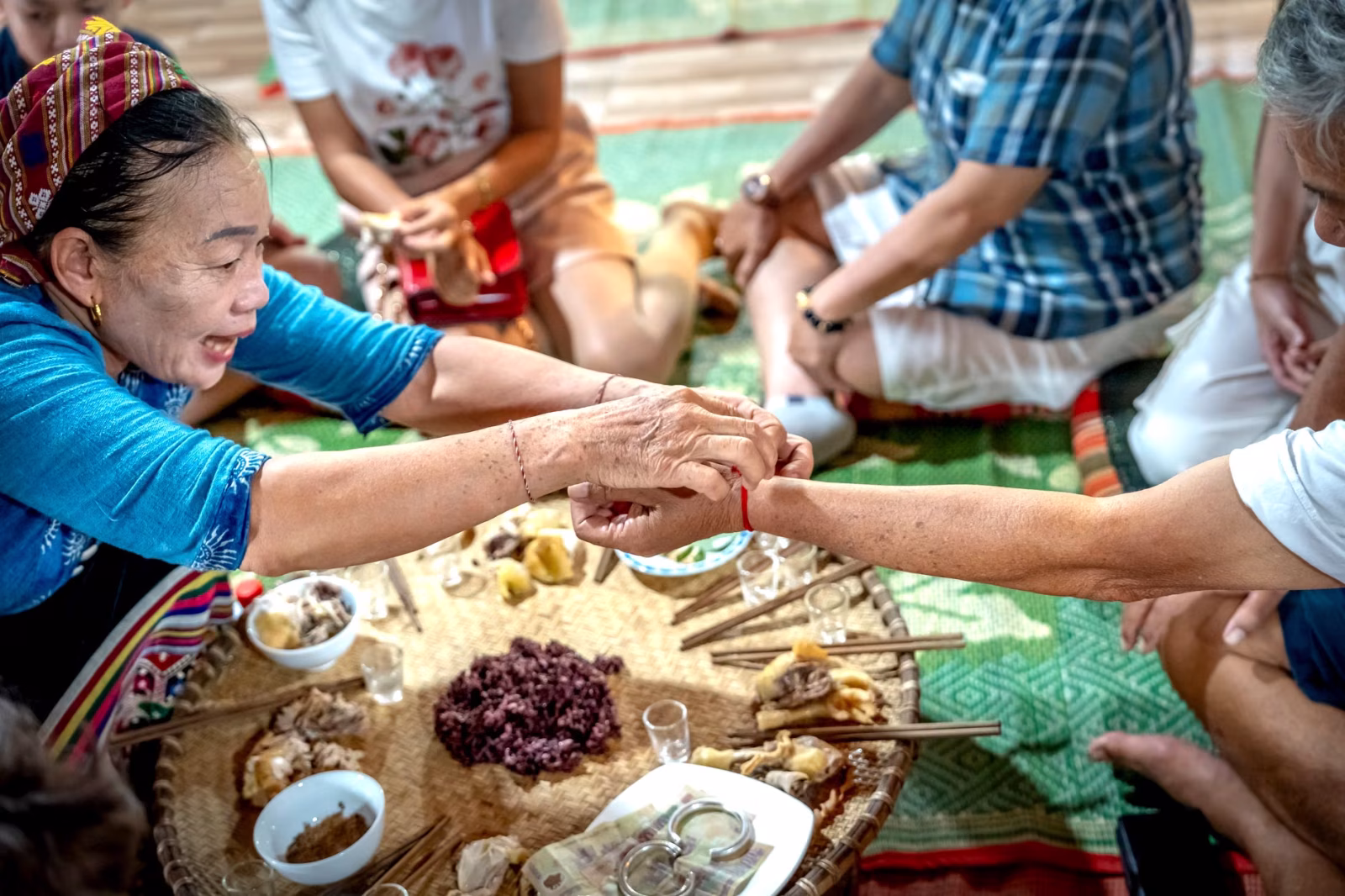 A group of adults share a traditional meal on a woven mat indoors.