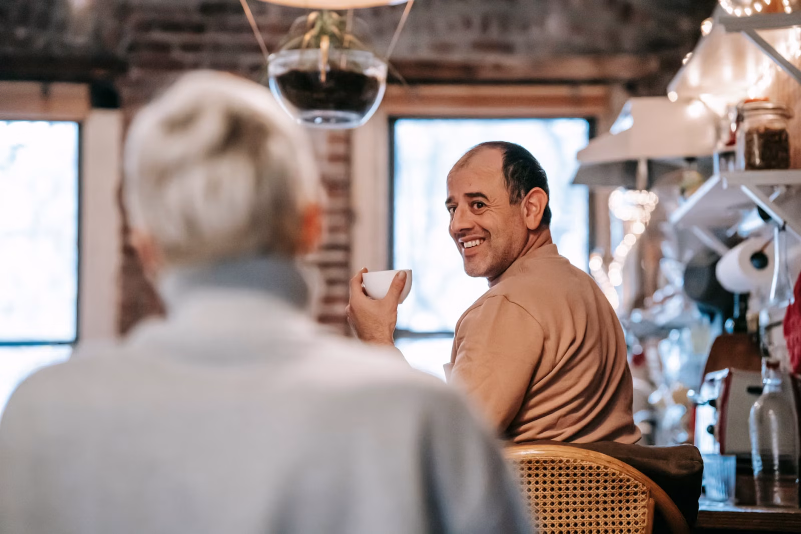 Back view of unrecognizable female in casual clothes speaking with happy middle aged ethnic husband drinking coffee at home