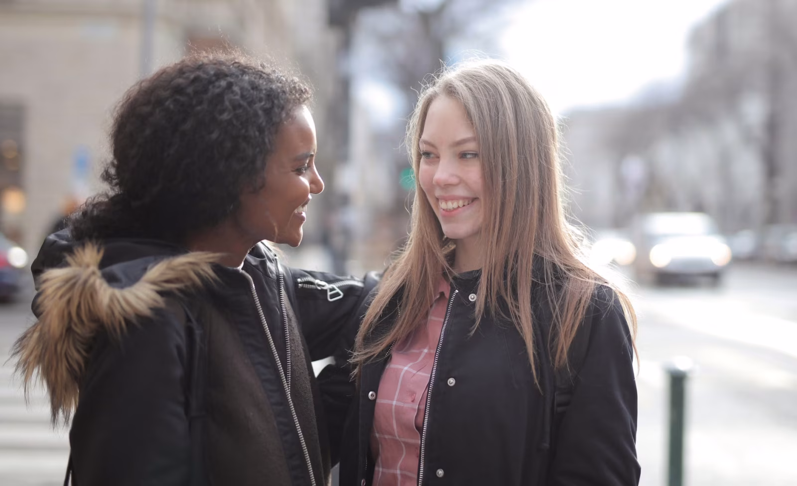 Two women in winter jackets happily interact outdoors, showcasing friendship and warmth.